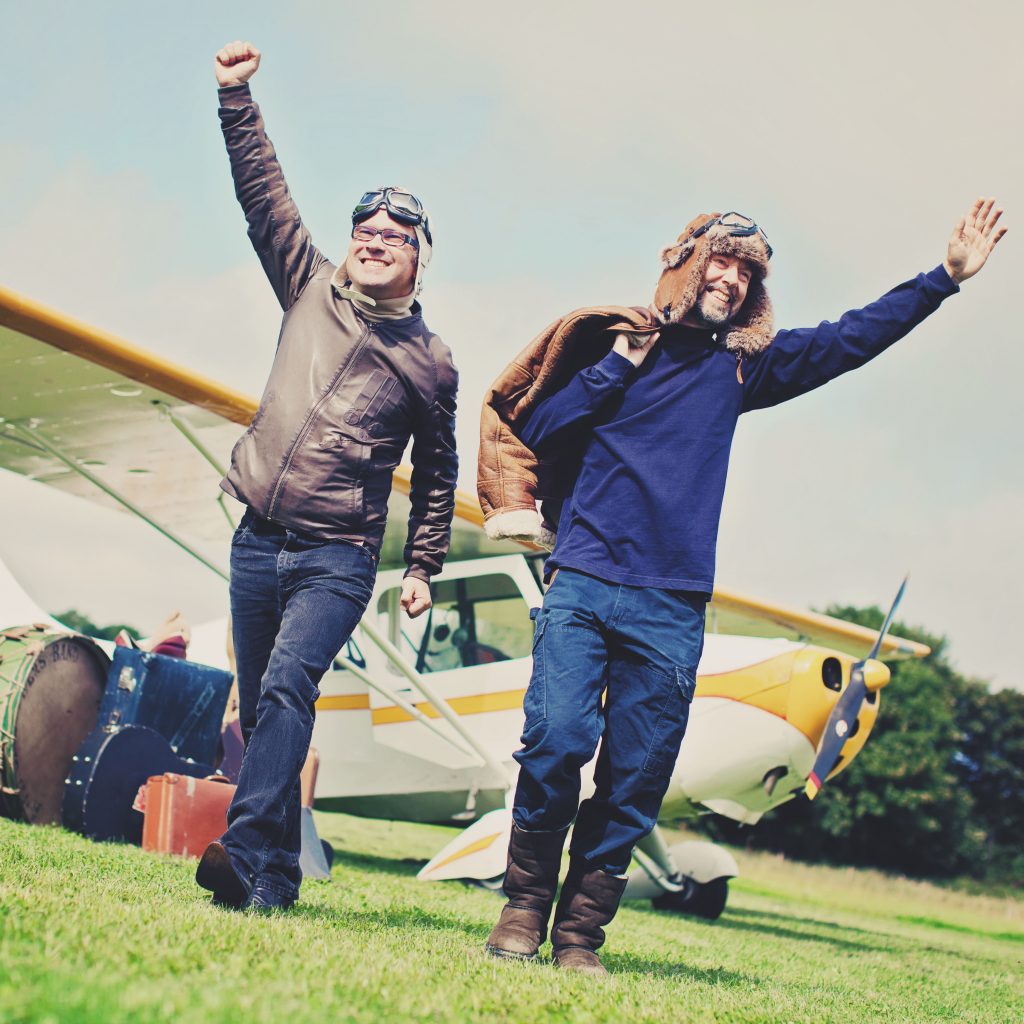 Leo and Anto emerge from a plane, wearing Biggles helmets