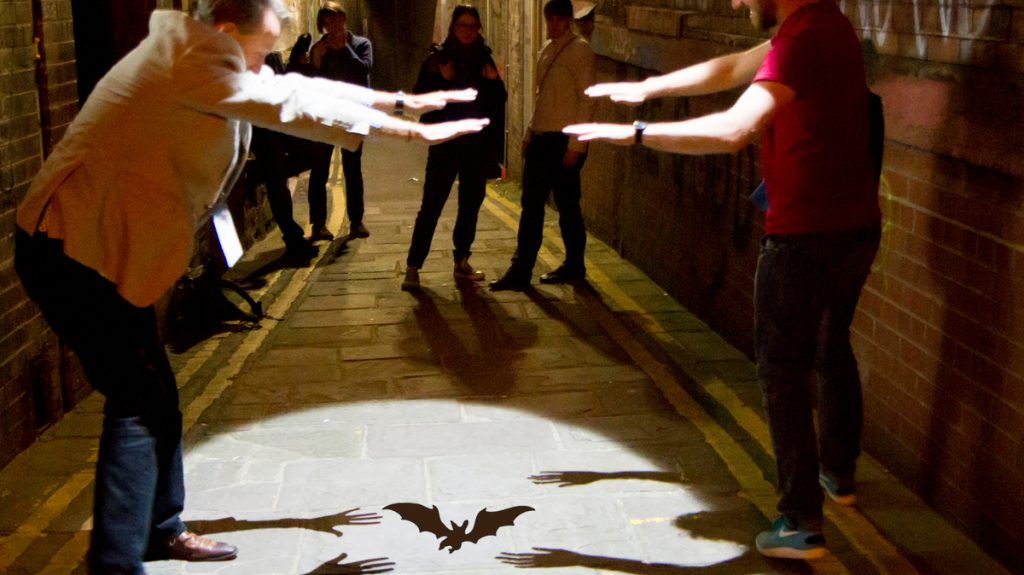 People create bat shadows beneath a Bristol lamp post