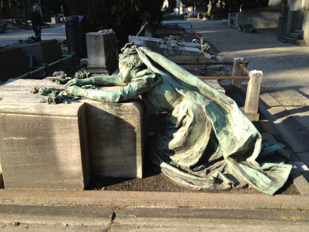 A dramatic green statue of a mourning women, draped over monument in Milan's 'city of the dead'