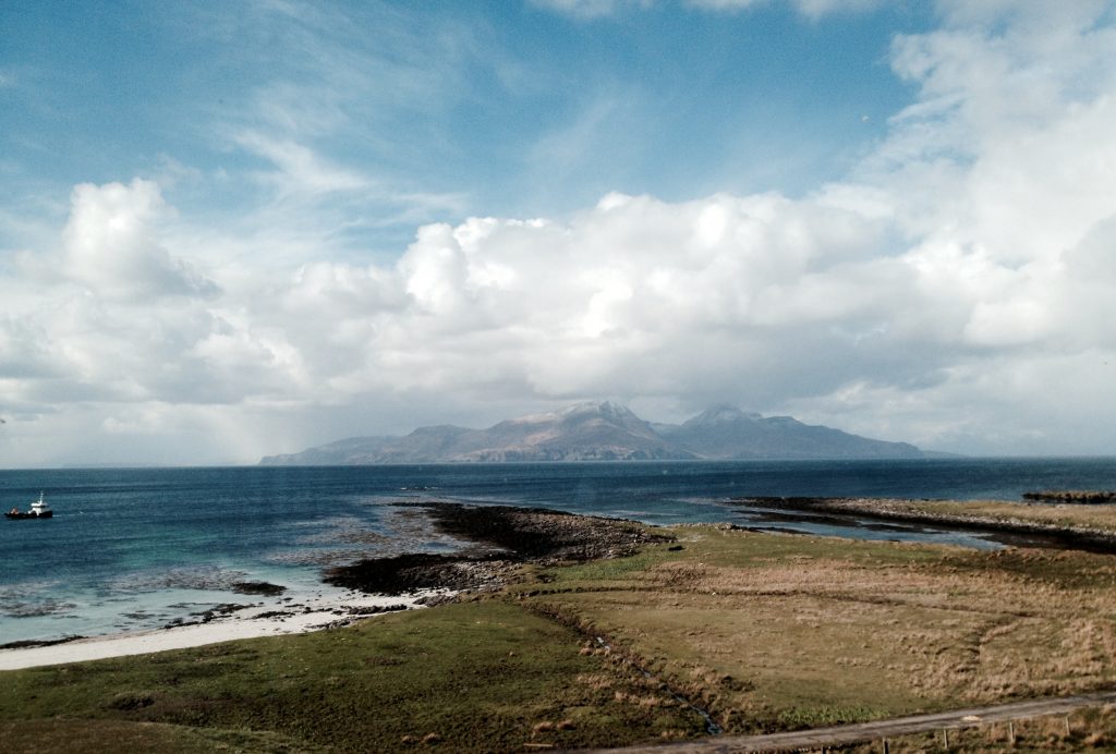 A view across the water to the Cuillins of Rum shrouded in misty cloud but with clear blue sky above